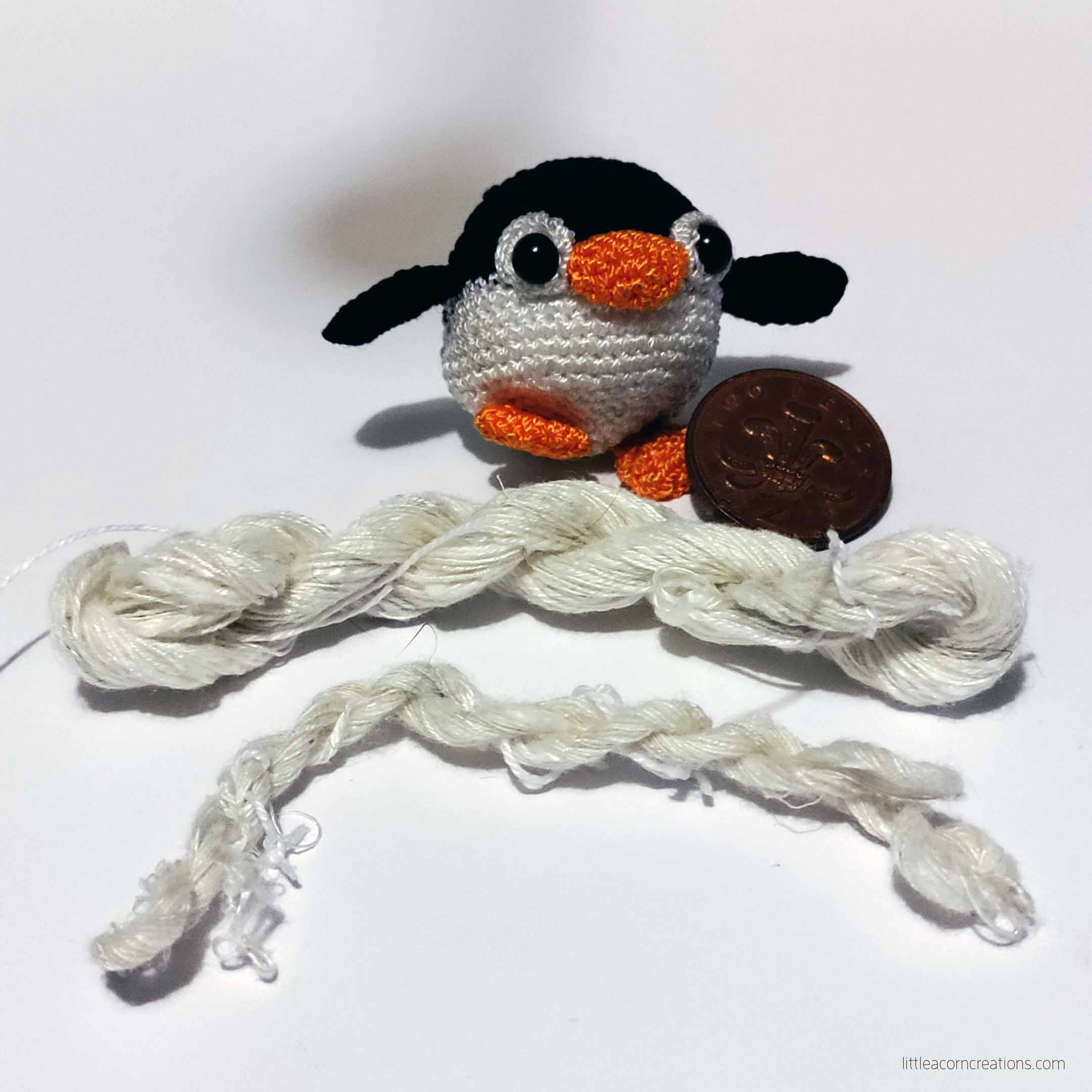 small amigurumi penguin, two pence coin, and two small skeins on handspin silk