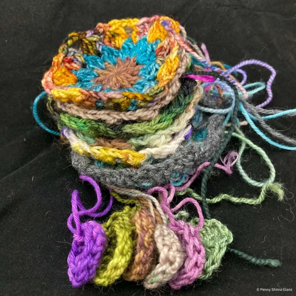 stack of multicolorful motifs in progress on a black background. in front are 6 centers, the stack includes the first 3 rounds for the "literary fragments blanket"