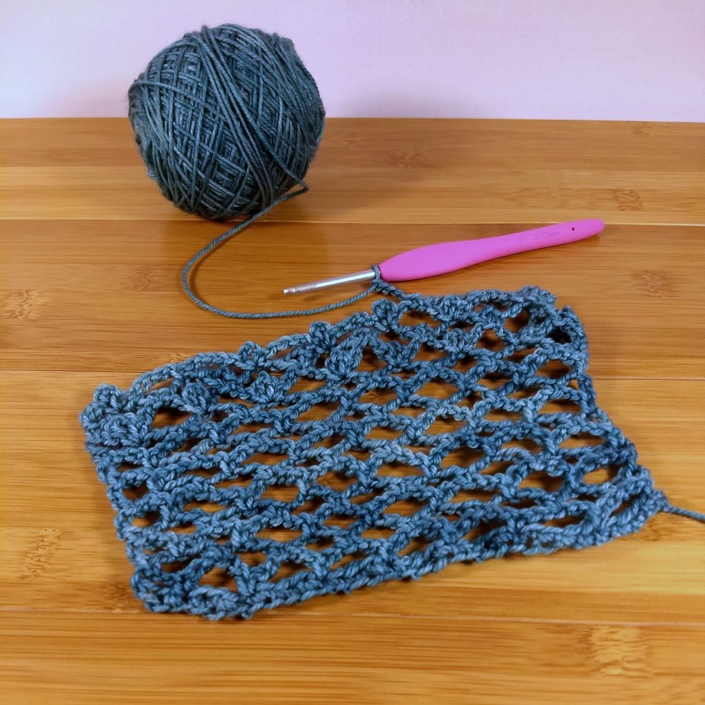 Anzula Squishy in a VLSI lace swatch, shown on the hook on a wooden surface.
