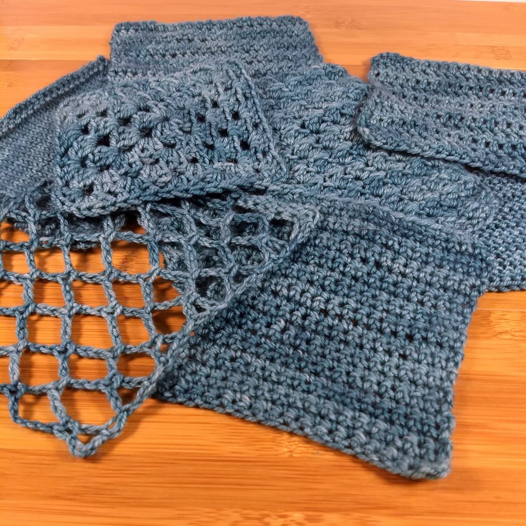 Various Anzula Squish swatches scattered in a layered by flat layout on a wooden surface. Both knit and crochet.