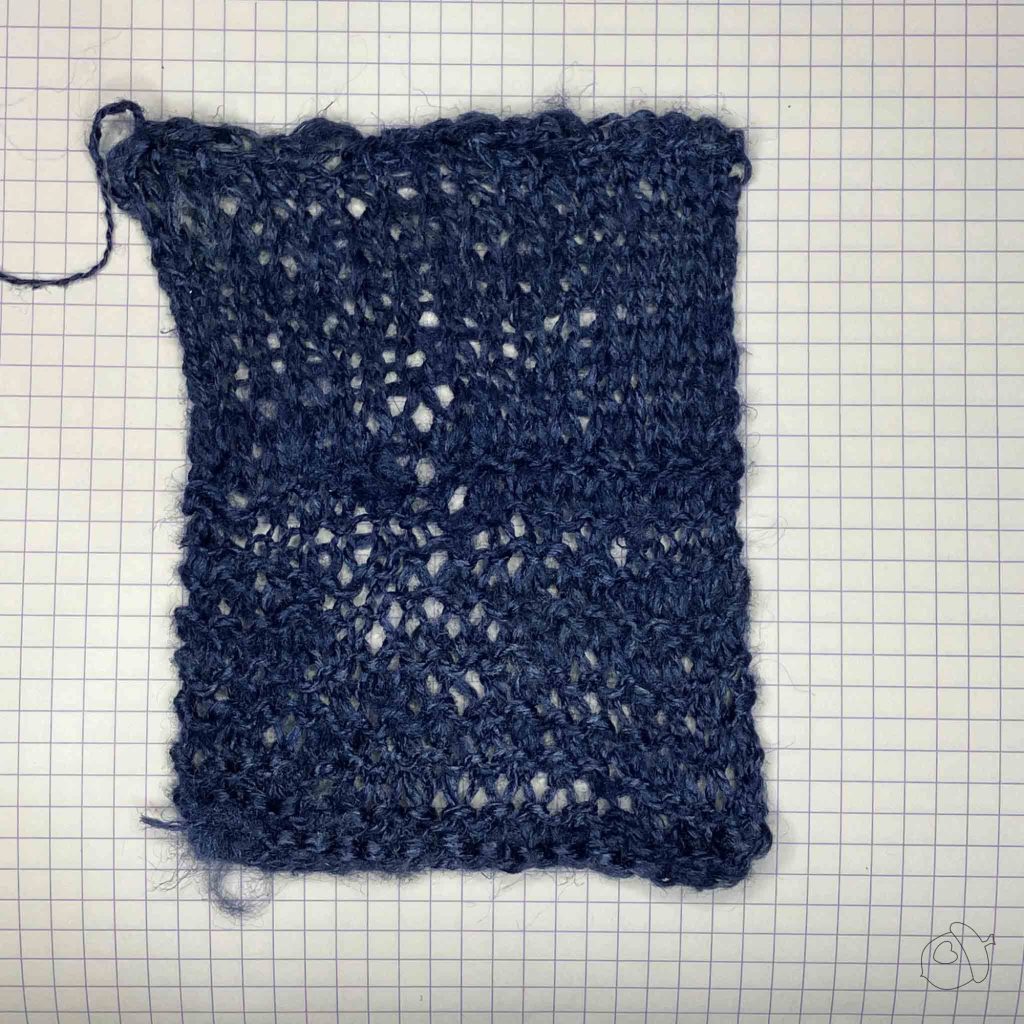 Knit stockinette and garter stitch swatch in ColourMart fingering weight crepe style silk bakketta, dark blue. blocked and laid flat on grid paper