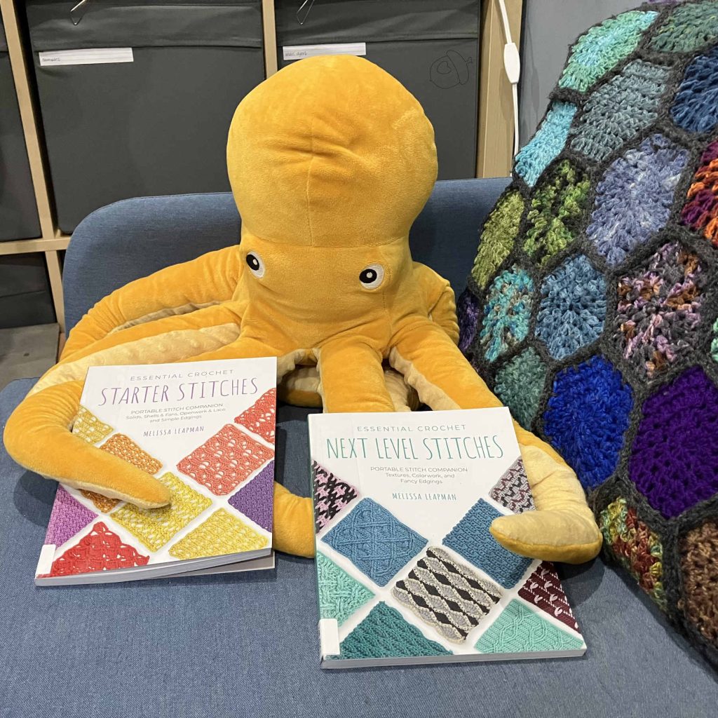 golden stuffed octopus toy and a light blue couch holding both Essential crochet books in its tentacles.