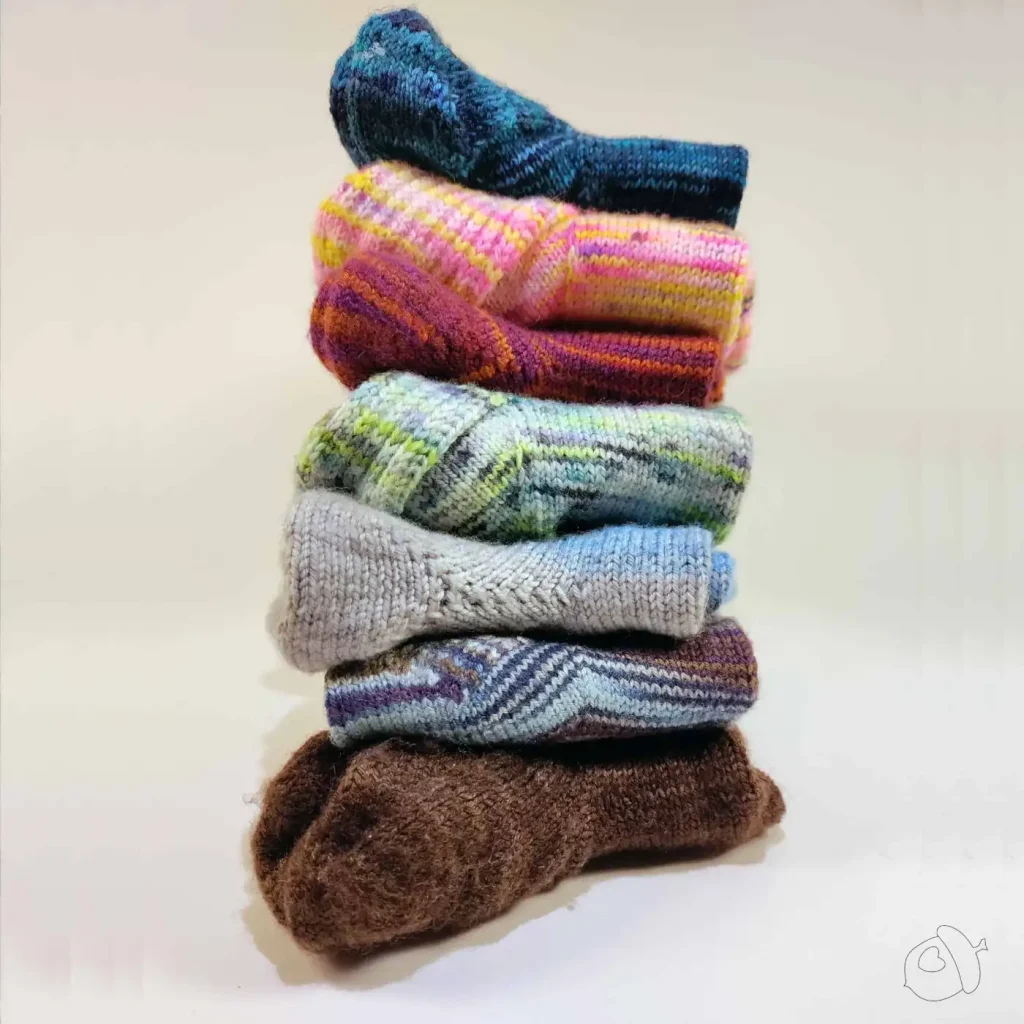 tower of 7 pairs of hand knit folded socks on a white background.