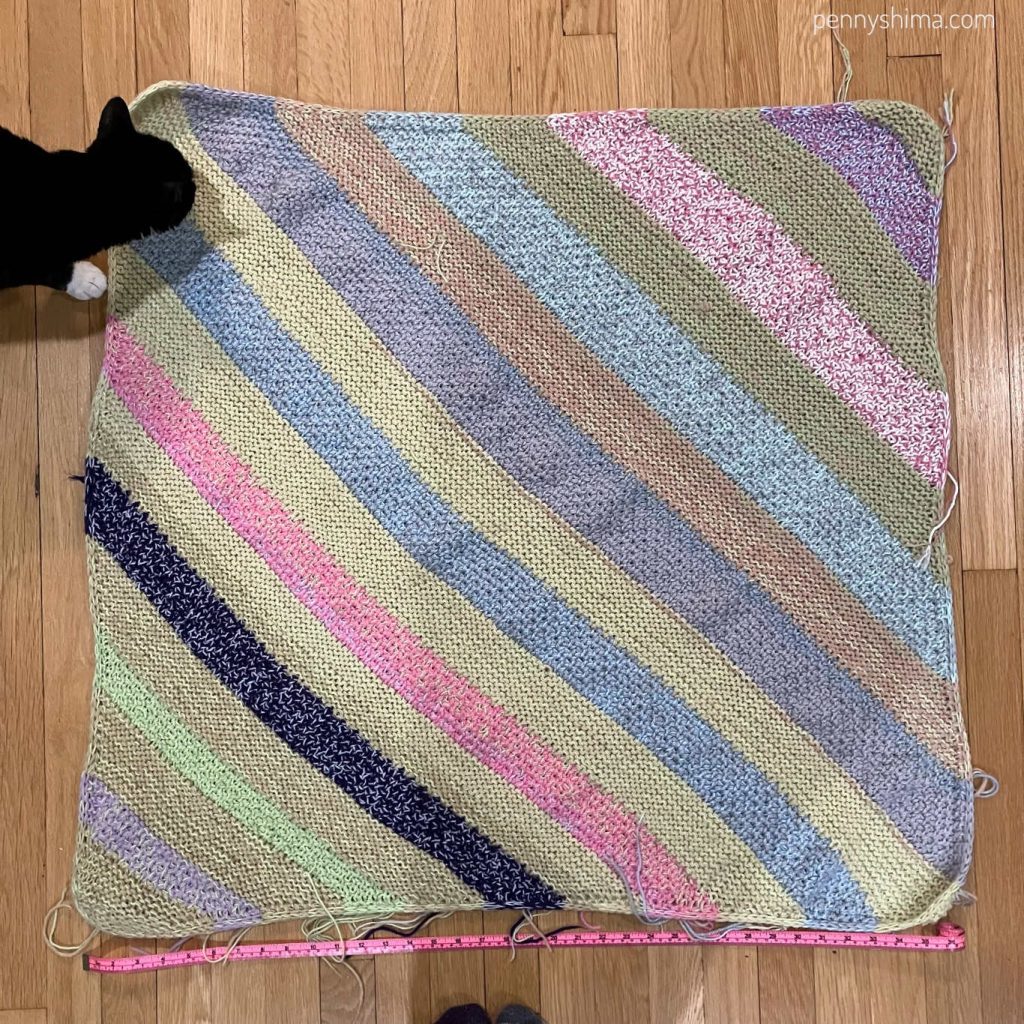 feline assistant dot inspecting the knit scrap yarn blanket. unblocked and without ends woven in.